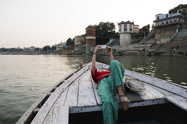 Западная женщина лежит на лодке и делает селфи в Варанаси